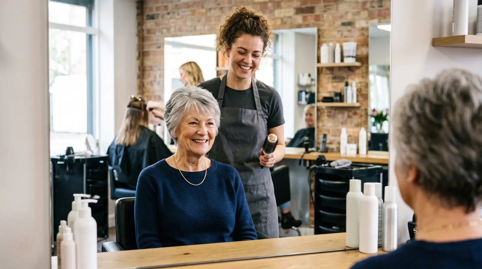 An older woman smiling at her fresh cut in the salon mirror, the hairdresser standing behind her